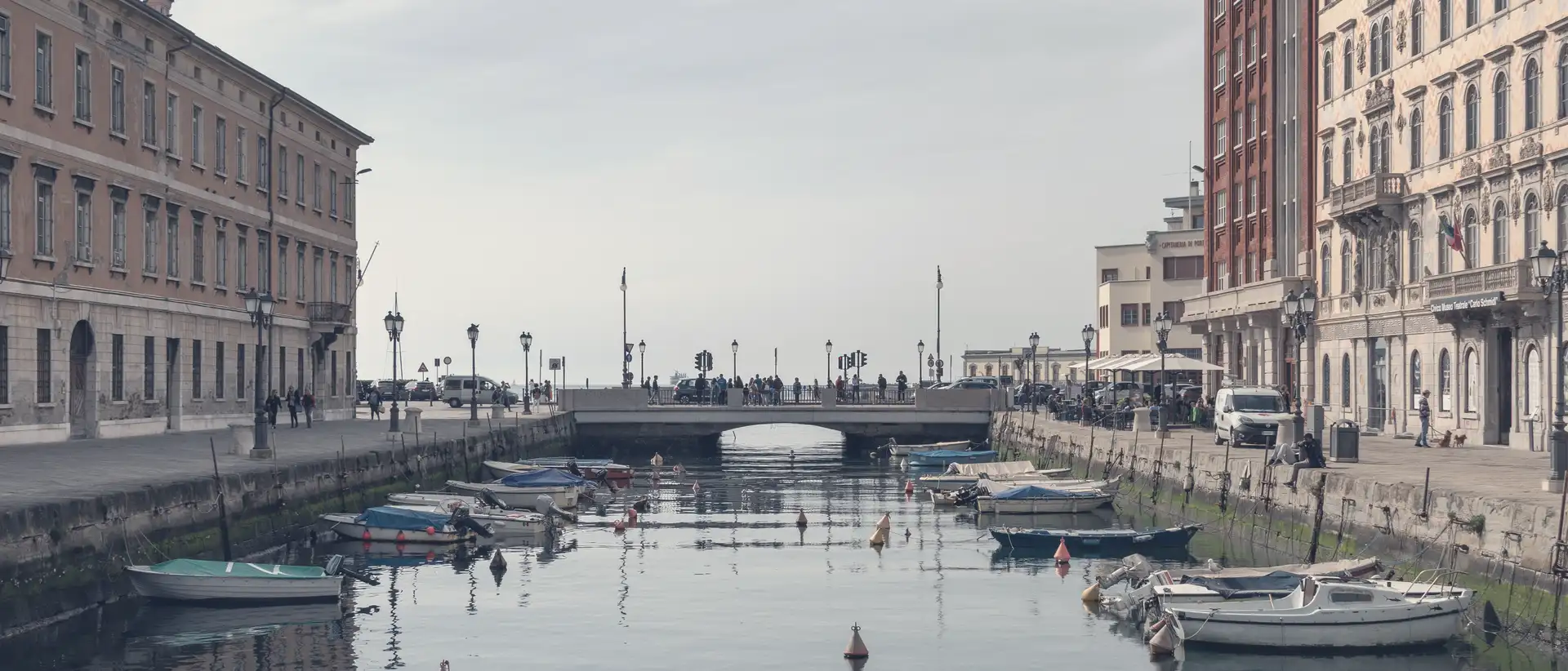 Il Canal Grande di Trieste con le barche ormeggiate, i palazzi ai due lati e il ponte in fondo.